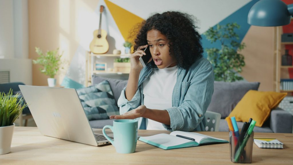 Femme au téléphone, l’air surpris et méfiant, devant son ordinateur