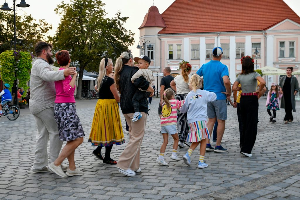 Adultes et enfants dansant en farandole sur une place de ville