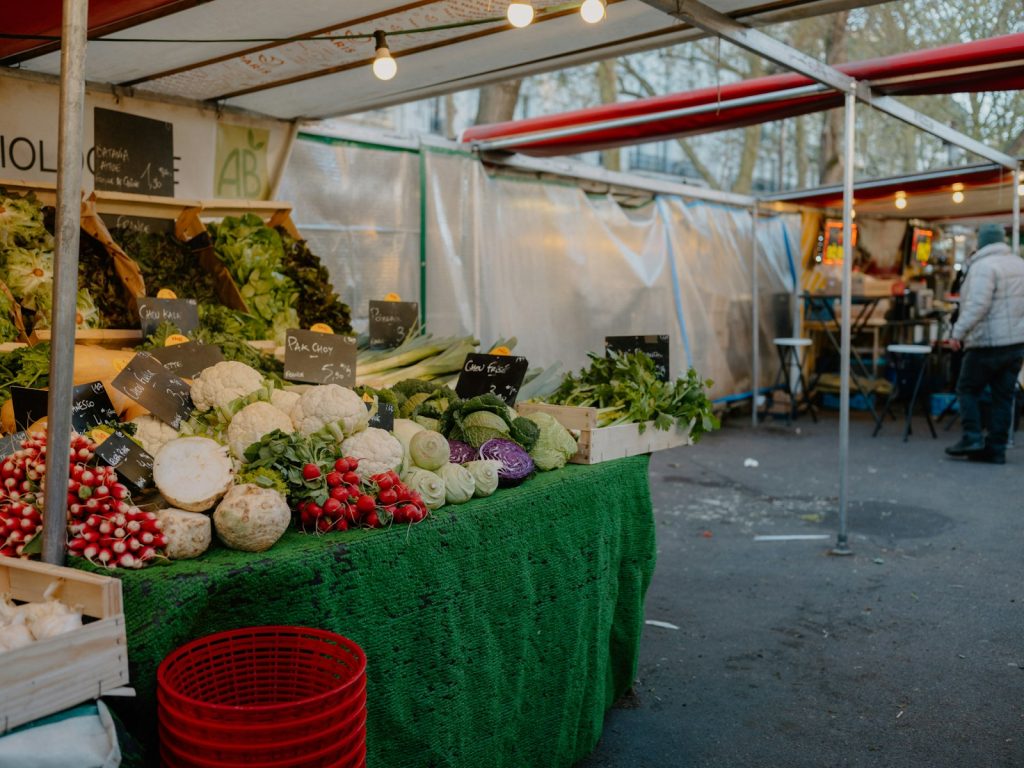 Étal de primeur sous les bâches d’un marché de plein air : choux-fleurs, radis, poireaux et salades