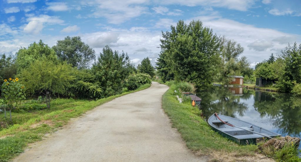 Chemin de promenade au bord de l’eau, une barque amarrée sur la berge, un jour d’été